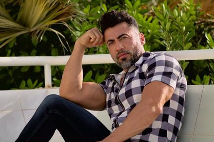 Pablo sentado en un banco, con camisa de cuadros, apoyando el brazo en la rodilla.