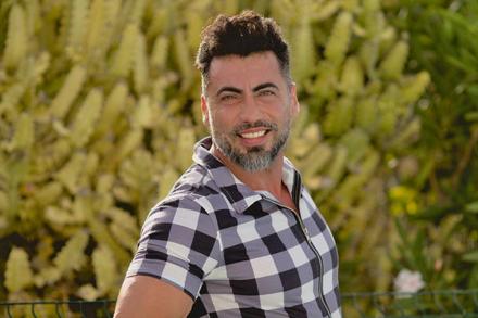 Retrato de Pablo sonriendo, con camisa de cuadros, en un exterior con vegetación.